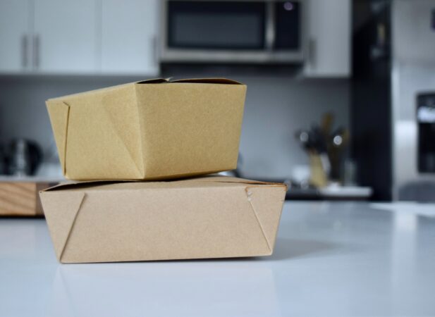 Boites repas en carton empilées sur une table de cuisine.